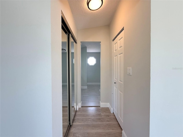 corridor with light wood-style floors, baseboards, and a textured ceiling