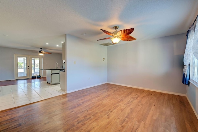 unfurnished living room with ceiling fan, sink, light hardwood / wood-style flooring, and a textured ceiling