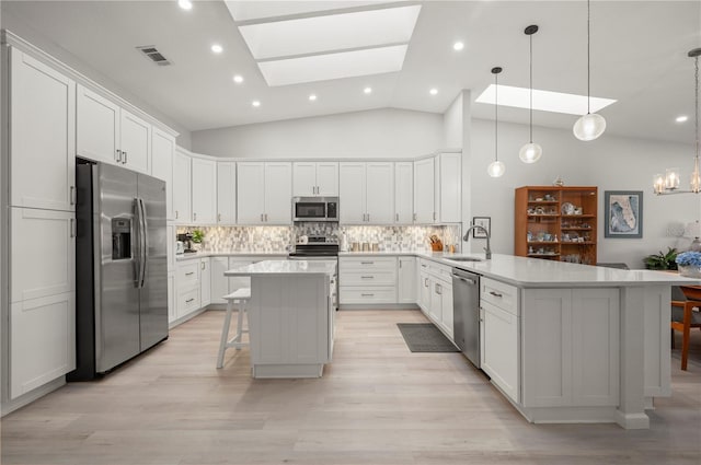 kitchen with kitchen peninsula, appliances with stainless steel finishes, backsplash, a kitchen bar, and a skylight