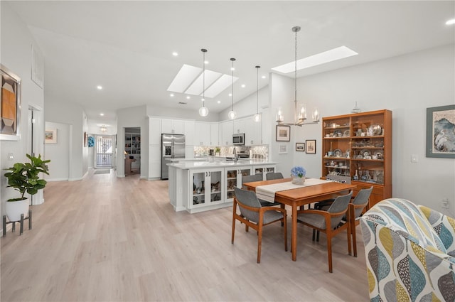 dining space with sink, light wood-type flooring, high vaulted ceiling, and a skylight