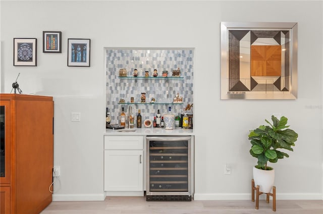 bar featuring decorative backsplash, white cabinets, beverage cooler, and light wood-type flooring