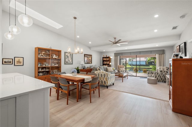 dining area featuring light wood-type flooring, ceiling fan with notable chandelier, and vaulted ceiling with skylight