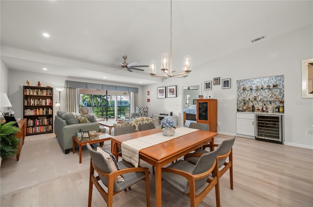 dining area featuring light hardwood / wood-style floors, ceiling fan with notable chandelier, bar area, and beverage cooler