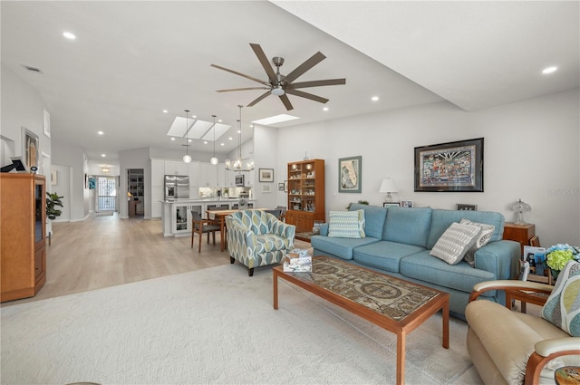 living room with ceiling fan with notable chandelier, light hardwood / wood-style flooring, and a skylight