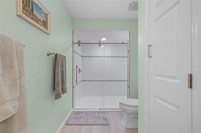 bathroom featuring hardwood / wood-style flooring, a shower with door, and toilet