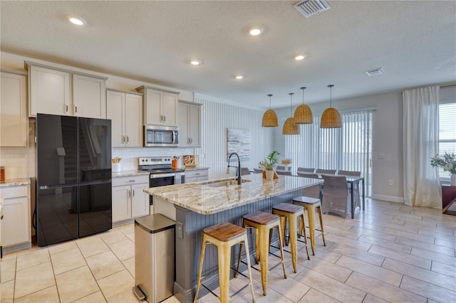 kitchen with sink, light stone counters, decorative light fixtures, appliances with stainless steel finishes, and a kitchen island with sink