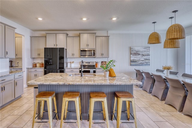 kitchen featuring appliances with stainless steel finishes, sink, gray cabinetry, and a kitchen island with sink