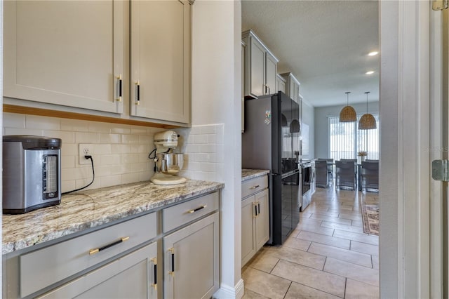 kitchen featuring decorative light fixtures, backsplash, light tile patterned floors, light stone counters, and black fridge