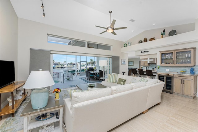 living room with high vaulted ceiling, beverage cooler, ceiling fan, and bar area