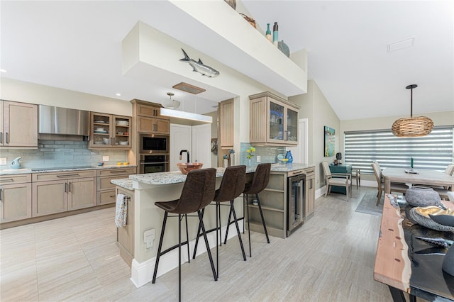 kitchen with wall chimney range hood, appliances with stainless steel finishes, a center island, decorative backsplash, and decorative light fixtures