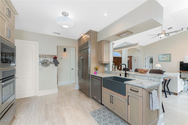 kitchen with light stone countertops, sink, built in appliances, and light brown cabinetry