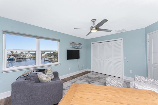 living room featuring dark hardwood / wood-style floors, ceiling fan, and a water view