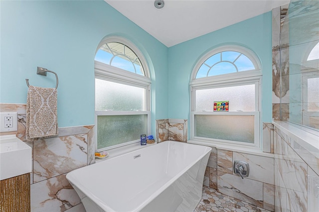 bathroom with vanity, a wealth of natural light, a bath, and tile walls