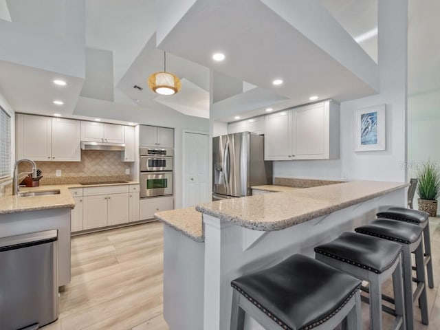 kitchen with light stone countertops, appliances with stainless steel finishes, sink, kitchen peninsula, and a breakfast bar area