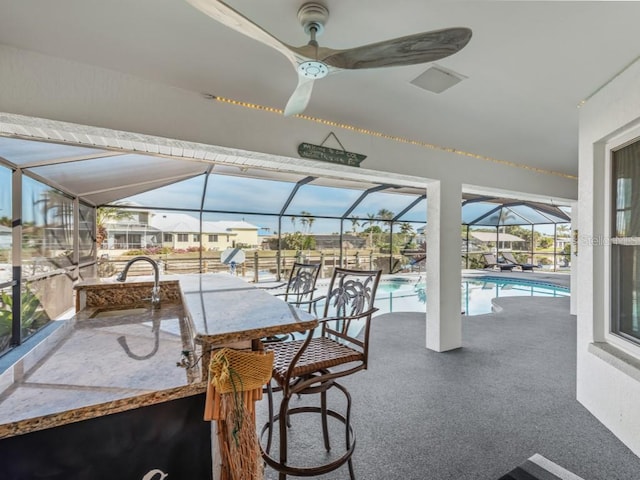 view of patio with glass enclosure, ceiling fan, and a wet bar