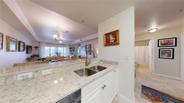 kitchen featuring light stone countertops, decorative light fixtures, white cabinetry, sink, and a tray ceiling