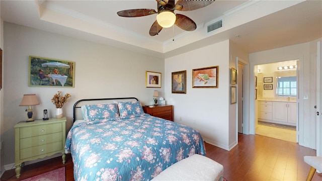 bedroom featuring crown molding, ceiling fan, a tray ceiling, hardwood / wood-style floors, and connected bathroom