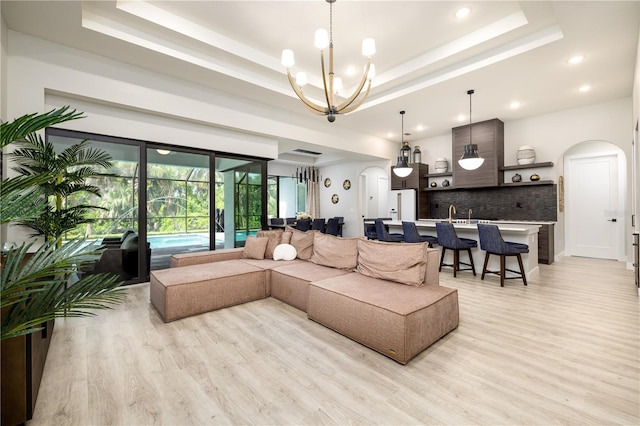 living room with light hardwood / wood-style floors, a tray ceiling, and an inviting chandelier