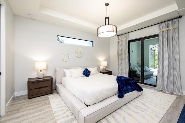 bedroom with light hardwood / wood-style floors, a tray ceiling, and access to outside