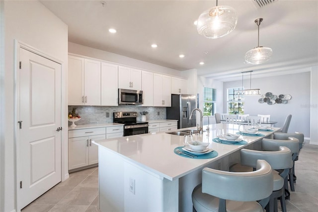 kitchen with a kitchen island with sink, hanging light fixtures, stainless steel appliances, and white cabinets