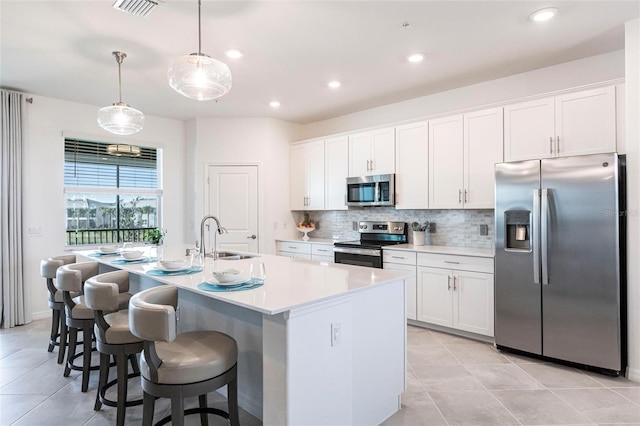 kitchen with sink, white cabinetry, hanging light fixtures, appliances with stainless steel finishes, and a kitchen island with sink