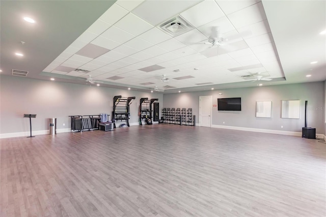 exercise area with ceiling fan, a tray ceiling, light hardwood / wood-style floors, and a drop ceiling