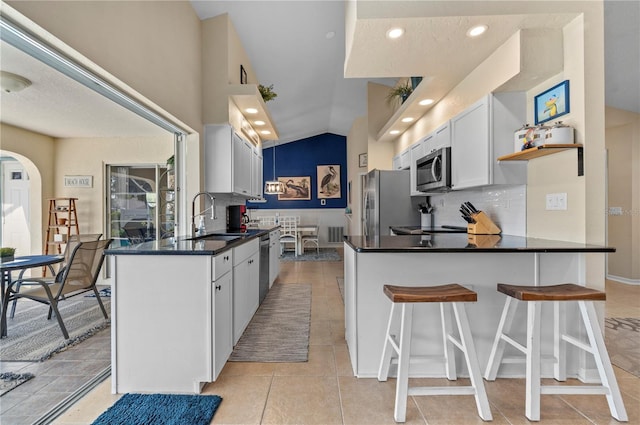 kitchen with vaulted ceiling, white cabinetry, decorative backsplash, sink, and stainless steel appliances