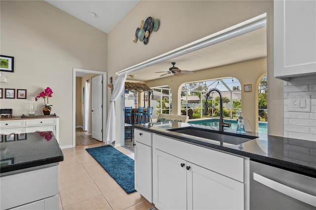 kitchen featuring white cabinetry, light tile patterned floors, stainless steel dishwasher, sink, and dark stone countertops