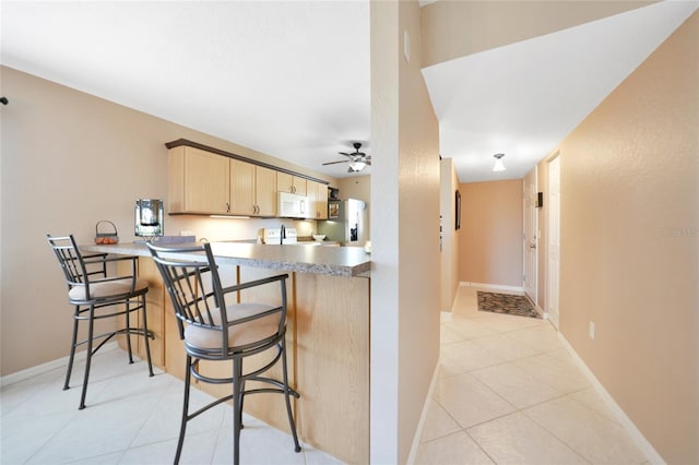 kitchen with a kitchen bar, light brown cabinetry, stainless steel fridge with ice dispenser, light tile patterned floors, and kitchen peninsula