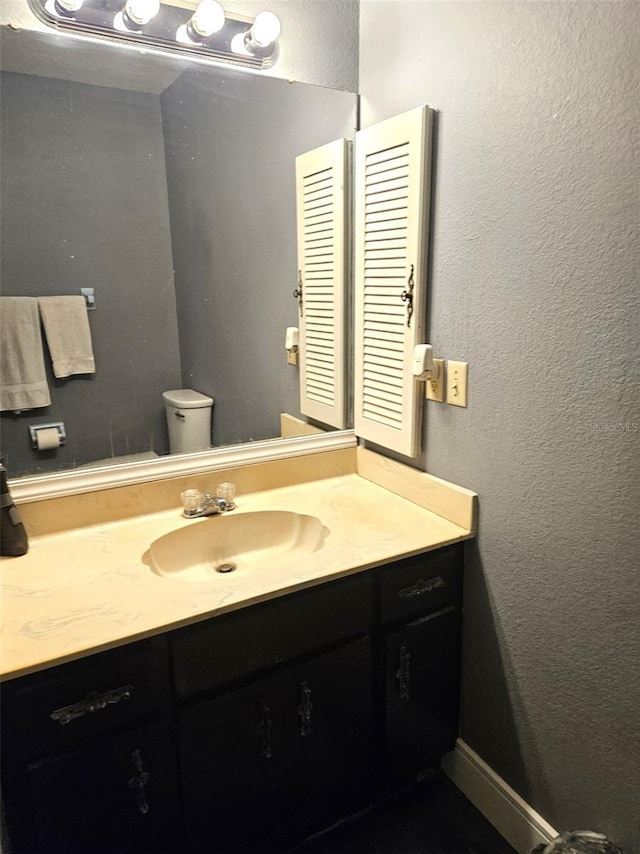 bathroom with a textured wall, vanity, and toilet