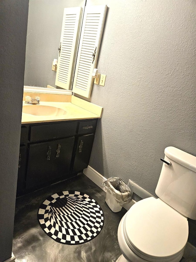 bathroom with a textured wall, toilet, concrete floors, vanity, and baseboards