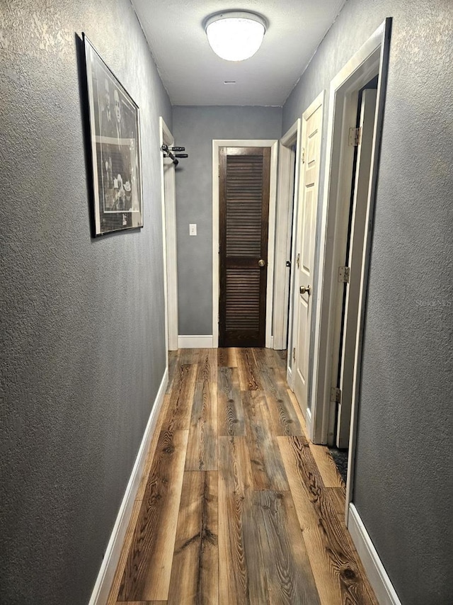 corridor featuring baseboards, wood finished floors, and a textured wall