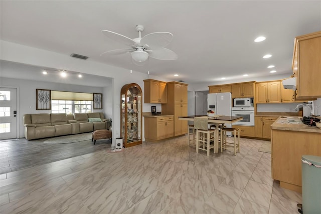 kitchen featuring sink, white appliances, a breakfast bar area, ceiling fan, and a kitchen island