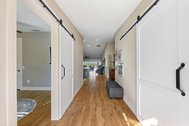 corridor with a barn door and light hardwood / wood-style floors