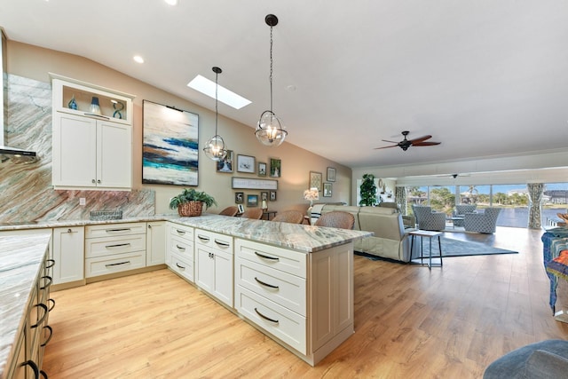 kitchen with lofted ceiling with skylight, hanging light fixtures, light wood-type flooring, light stone countertops, and white cabinets