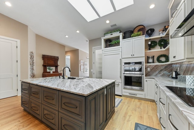 kitchen with dark brown cabinetry, white cabinetry, light stone counters, ventilation hood, and an island with sink