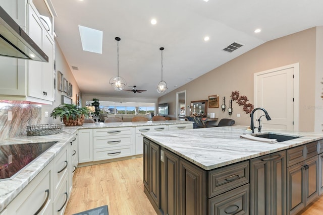 kitchen featuring dark brown cabinetry, sink, light stone counters, decorative light fixtures, and white cabinets