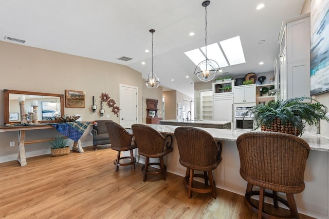 kitchen featuring a breakfast bar area, hanging light fixtures, light stone counters, light hardwood / wood-style floors, and white cabinets