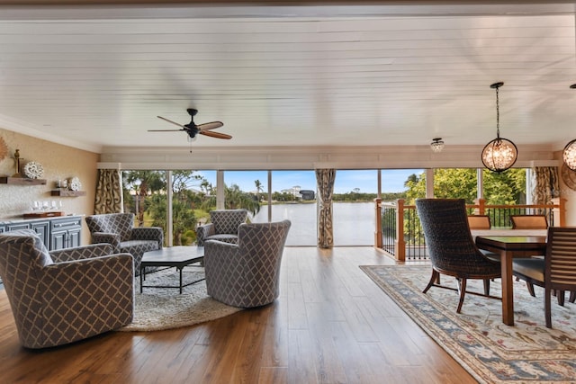 living room featuring hardwood / wood-style floors, ceiling fan with notable chandelier, ornamental molding, and a water view