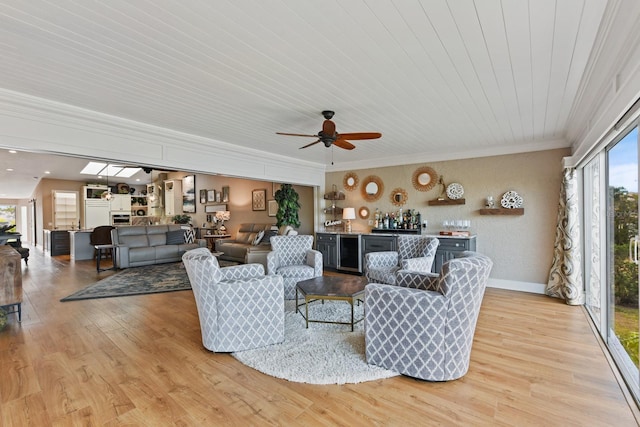 living room featuring bar, crown molding, light hardwood / wood-style flooring, ceiling fan, and beverage cooler