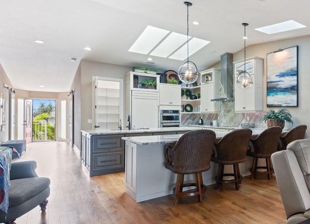 kitchen with gray cabinets, a skylight, hanging light fixtures, light stone countertops, and wall chimney exhaust hood