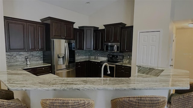 kitchen featuring tasteful backsplash, stainless steel appliances, kitchen peninsula, and a kitchen bar