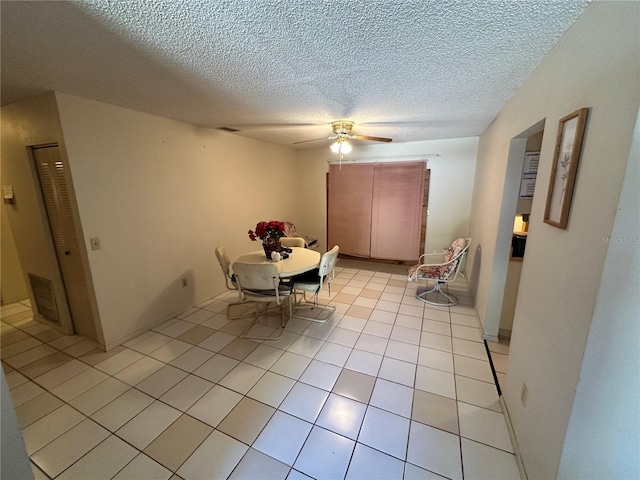 unfurnished dining area with ceiling fan, light tile patterned floors, and a textured ceiling