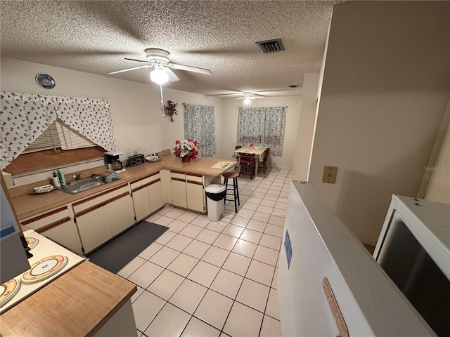 kitchen with light tile patterned flooring, sink, ceiling fan, kitchen peninsula, and a textured ceiling