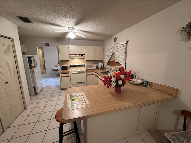 kitchen with white appliances, a breakfast bar area, cream cabinets, a textured ceiling, and kitchen peninsula