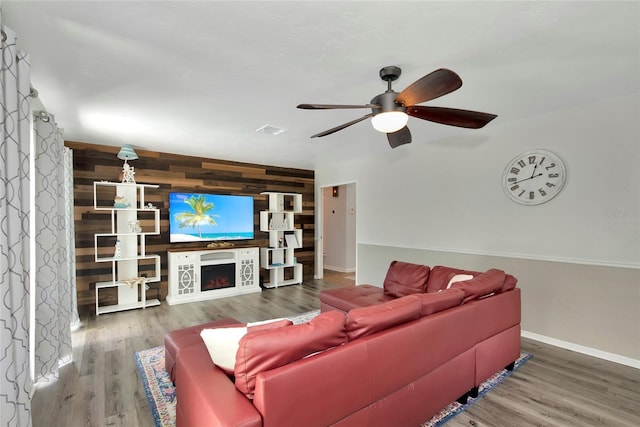 living room featuring hardwood / wood-style flooring, wood walls, ceiling fan, and a fireplace