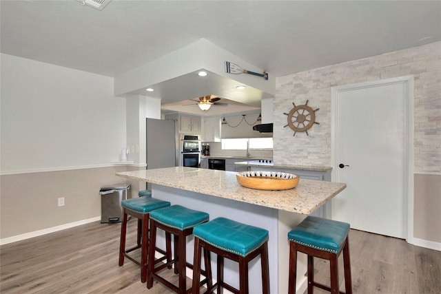 kitchen with hardwood / wood-style floors, light stone countertops, a kitchen bar, sink, and stainless steel appliances