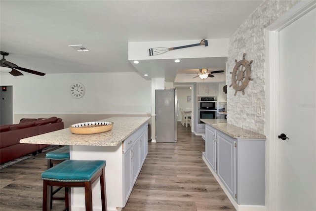 kitchen featuring white cabinets, a center island, stainless steel appliances, a kitchen breakfast bar, and light wood-type flooring