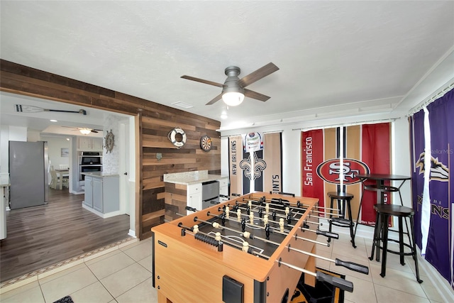 playroom featuring ceiling fan, wooden walls, and light tile patterned flooring