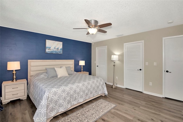 bedroom with ceiling fan, dark wood-type flooring, a textured ceiling, and two closets